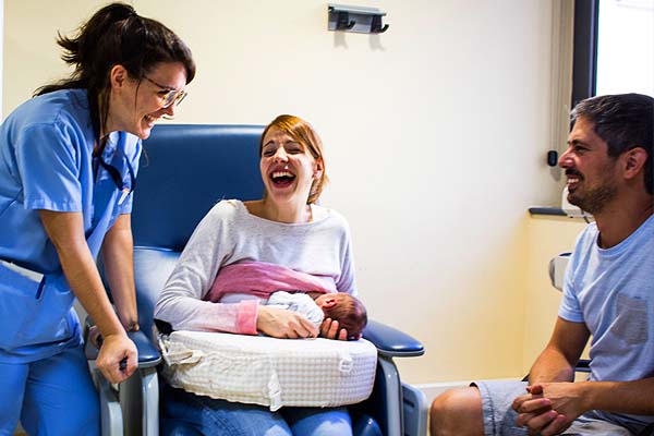 Uns pares i una llevadora somrient mentre la mare està donant el pit a un bebè.